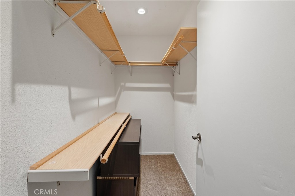 Walk-in closet with wood shelving and hanging rods along both sides, a dark dresser, and carpeted floor.