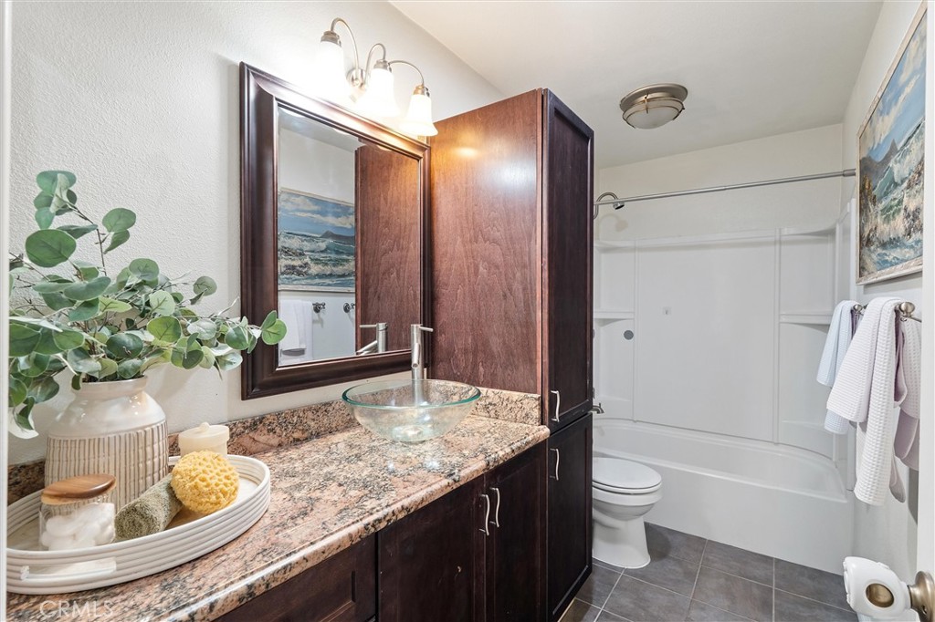 Bathroom with a granite vanity, glass vessel sink, dark wood cabinets, toilet, and a tub-shower combination.
