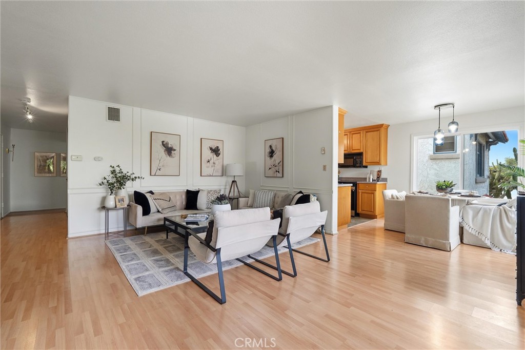 Open-plan living room and kitchen at 372 Carroll E 201, with light wood floors, a white sectional and armchairs, framed wall art, and warm wood cabinetry.