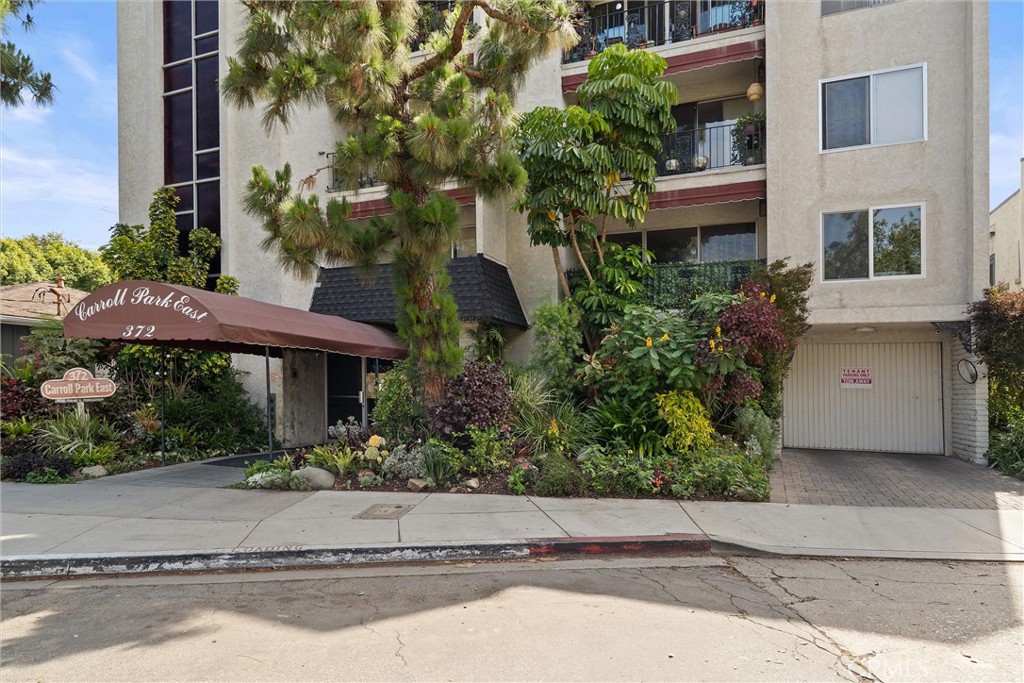 Street-level view of the beige condominium building at 372 Carroll E, with a covered entrance, landscaped gardens, balconies, and a garage.