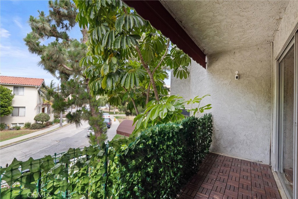 Covered balcony at 372 Carroll E 201 with brick pavers, leafy trees, and a hedge overlooking a residential street.