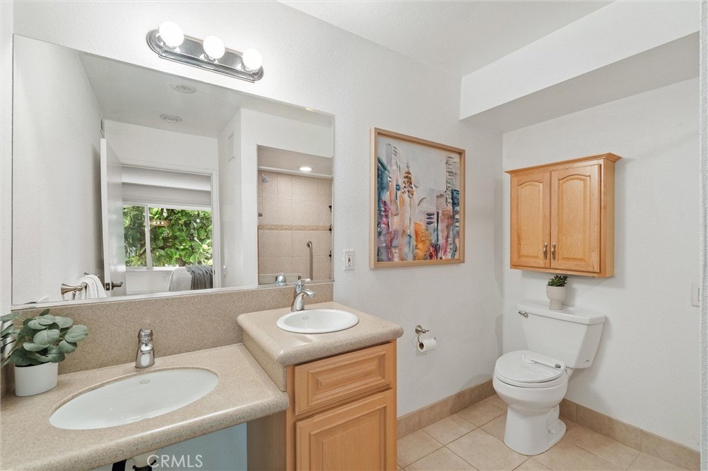 Bright bathroom with a long beige double-sink vanity, large mirror, toilet, and wooden wall cabinet.