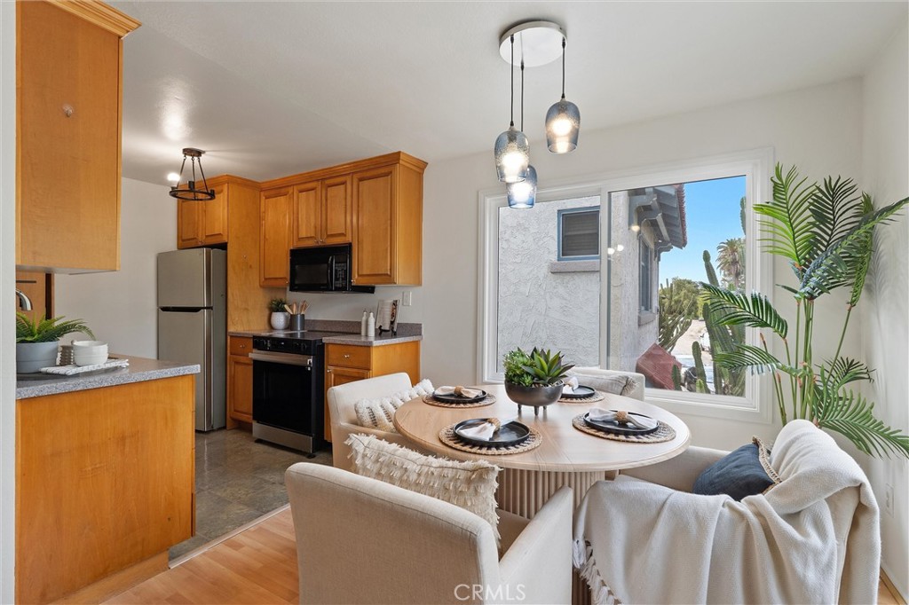 Open-plan kitchen and dining area at 372 Carroll E 201, with warm wood cabinets, stainless steel appliances, a round dining table, and large windows beside indoor plants.