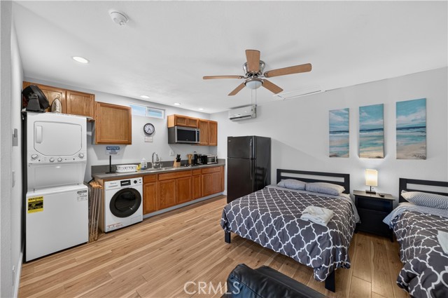 A studio apartment featuring a small kitchen area with wooden cabinets, a stacked washer and dryer, and two beds.