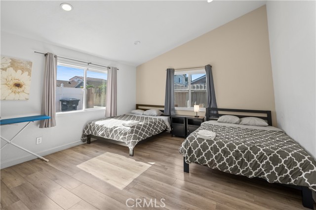 A bedroom with two beds, wood-look flooring, and a vaulted ceiling.