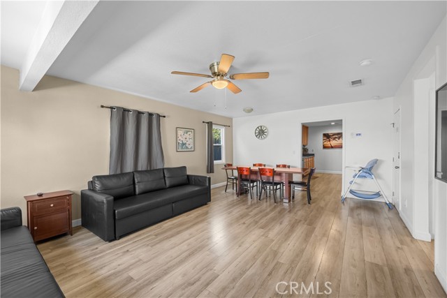 A living room with light wood flooring, a black sofa, and a dining table in the background.