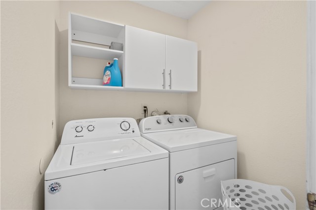 A laundry room with white washer and dryer, white cabinets, and laundry basket