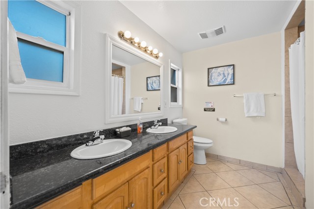 A full bathroom with a long wooden double vanity, granite countertop, two sinks, and a large mirror.