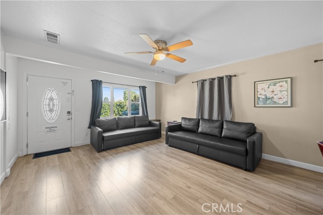Living room with light wood flooring, two leather sofas, a front entry door, and a ceiling fan.