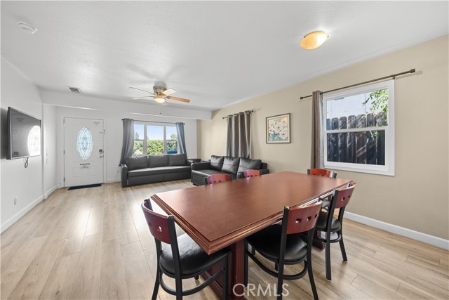 A living room and dining room combo with wood-look floors, a leather sofa, and a dining table.