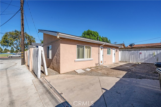 Exterior side view of a small single-story residential building with beige stucco walls and concrete driveway area