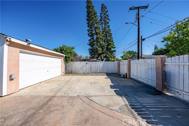 A detached garage with a white roll-up door next to a concrete driveway and a white wooden fence.