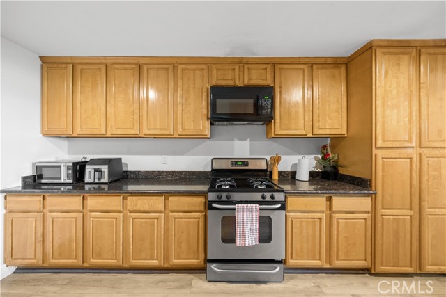 A kitchen with light wood cabinets, dark granite countertops, stainless steel gas stove, and over-the-range microwave.
