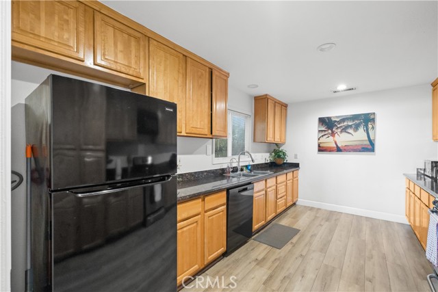 A kitchen featuring light wood cabinetry, dark countertops, black appliances, and light wood-look flooring.