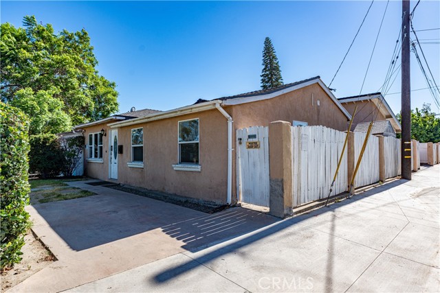 Exterior side view of a beige stucco house with a white wooden fence and concrete driveway