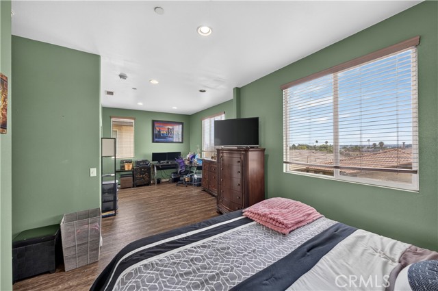 A bedroom with green walls, a bed in the foreground, and an office workspace in the background.