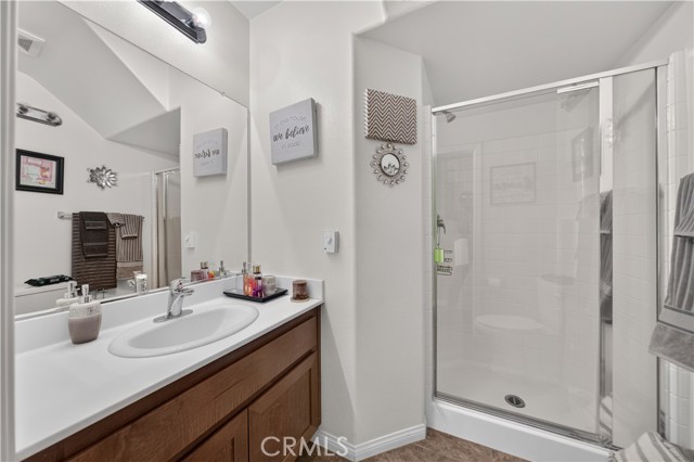 A standard bathroom with a white vanity sink, a large wall mirror, and a walk-in shower stall with glass doors.