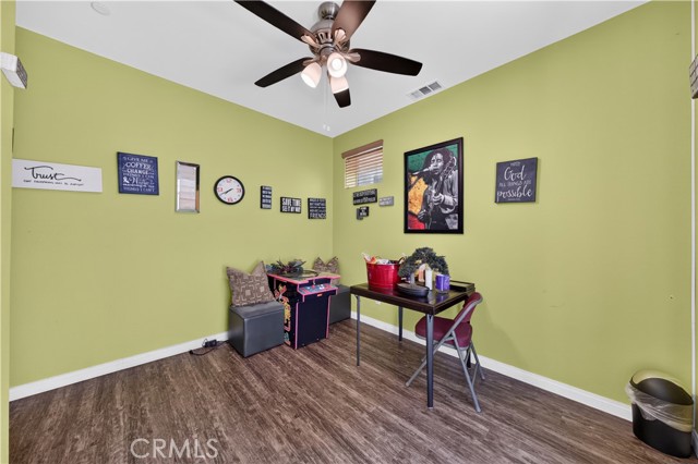 A small game room with light green walls, wood-look flooring, a ceiling fan, a small desk with a chair, and a compact arcade cabinet.
