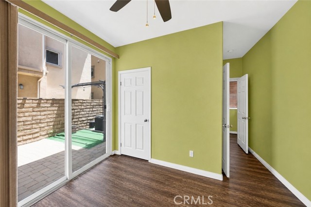 A vacant bedroom with olive green walls, dark wood-look flooring, a ceiling fan, and sliding glass doors leading to a small brick patio.