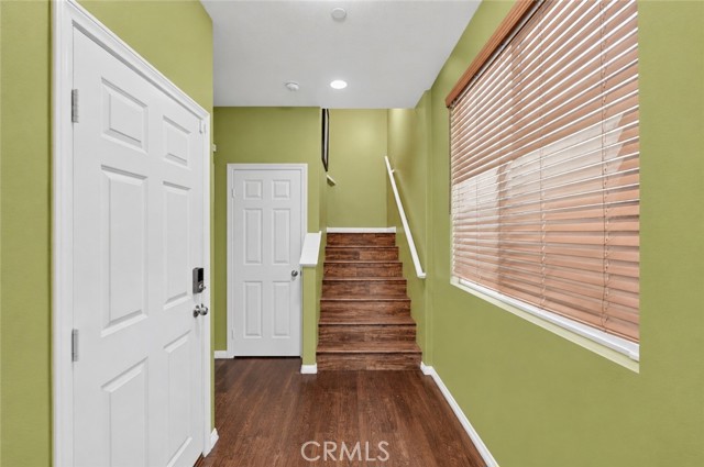 An entry hallway with green walls, wood floors, a white front door, and a wooden staircase.