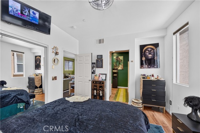 A bedroom with a dark blue bed, a mirrored closet door reflecting the room, wall art, and a TV mounted high on the wall