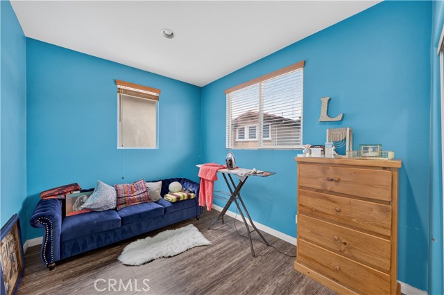 A bedroom featuring vibrant blue walls, a dark blue tufted sofa, a wooden dresser, and an ironing board setup.