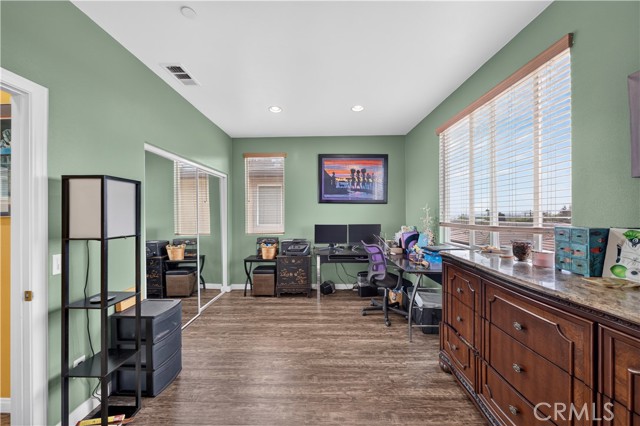 A home office featuring light green walls, a large wooden dresser, a computer workstation with dual monitors, and mirrored sliding closet doors.