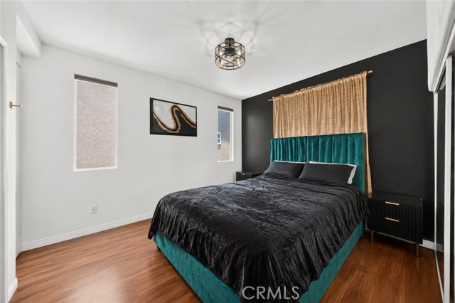 A modern bedroom featuring a teal velvet upholstered bed, a dark accent wall, and wood-style flooring.