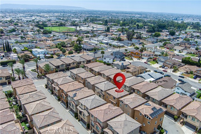 An aerial drone view of a dense suburban housing development with a red map location marker pointing to one of the units.