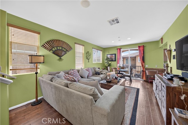 A furnished living room with light green walls, a large grey sectional sofa, and hardwood flooring.