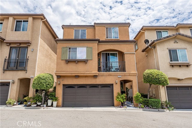 Exterior shot of a three-story beige townhouse featuring a garage, a balcony, and brown window shutters.