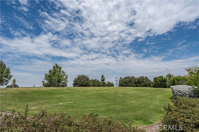 A wide-angle view of a large, grassy residential lot under a blue sky with scattered clouds.