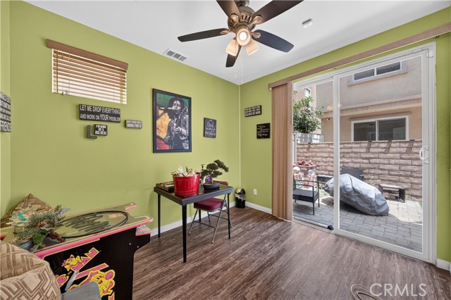 A den room featuring light green walls, a ceiling fan, wood-look flooring, an arcade cabinet, a small desk, and sliding glass doors leading to a patio.