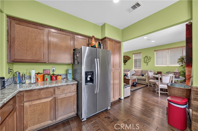 A kitchen with wooden cabinets, stainless steel refrigerator, and granite countertops opening into a living space