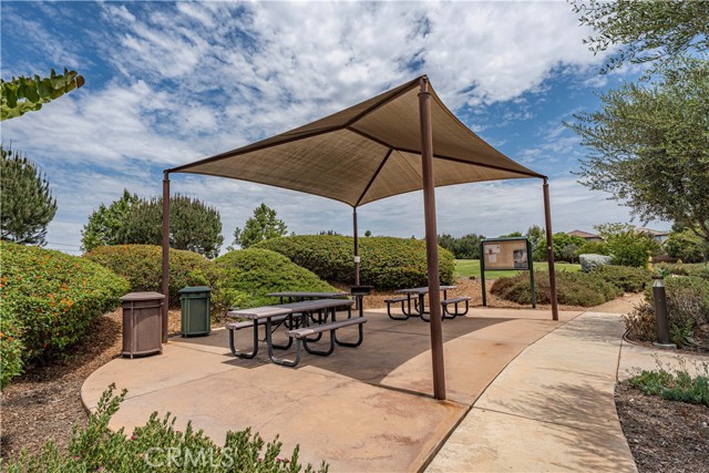 Outdoor community picnic area with metal tables and a large shade structure surrounded by landscaping.