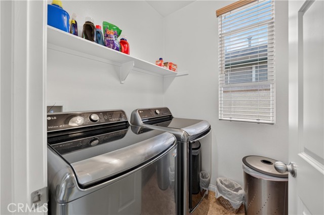 A small laundry room featuring a washer and dryer, white walls, and a shelf with laundry detergents.