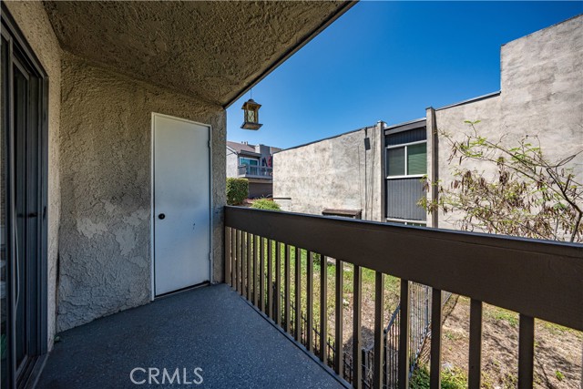 A covered outdoor balcony overlooking a grassy area and neighboring stucco buildings.