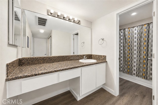 A clean, well-lit bathroom vanity with granite countertop and mirror, adjacent to a shower area with a patterned curtain.