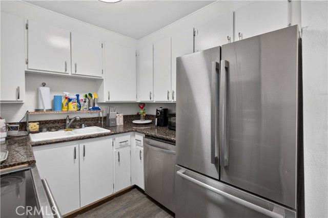 A kitchen with white cabinets, dark granite countertops, and stainless steel refrigerator and dishwasher.