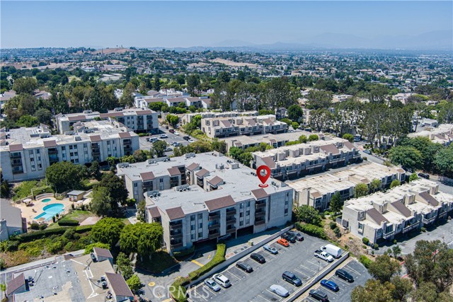 Aerial view of a multi-story apartment complex with a red location pin pointing at a specific building, featuring a swimming pool, parking lot, and surrounding neighborhood.