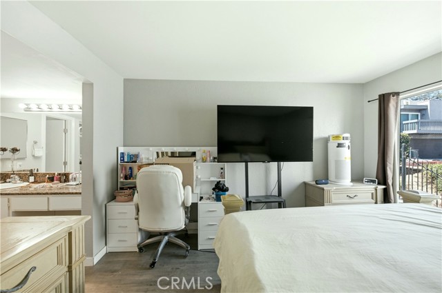 A bedroom featuring a white desk with a chair, a large wall-mounted TV, a dresser with an air purifier, and an attached bathroom entrance.