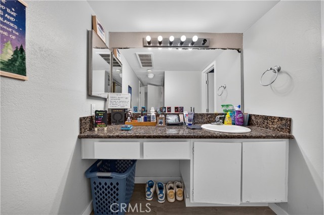 A bathroom vanity with a granite countertop, single sink, large mirror, and open storage underneath.