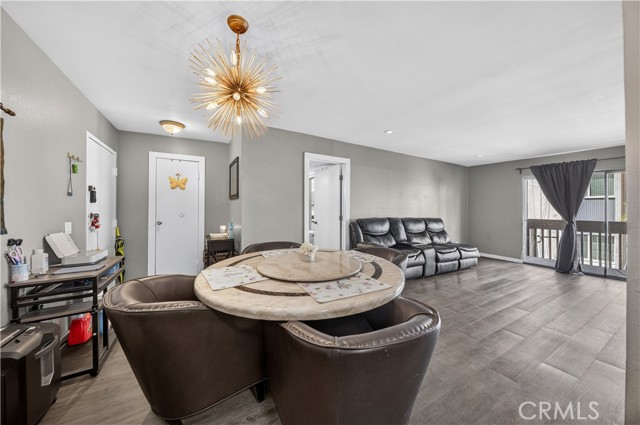 A living room with grey walls, dark wood-style flooring, a dining set, and a black leather sofa.