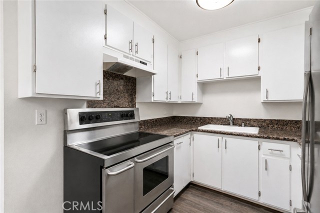 A clean kitchen with white cabinets, dark granite countertops, and stainless steel range.