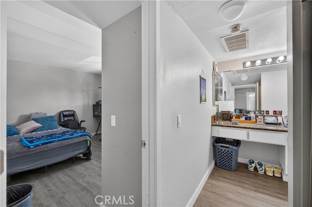 A view from a doorway looking into a bedroom with a bed and a vanity station on the right side.