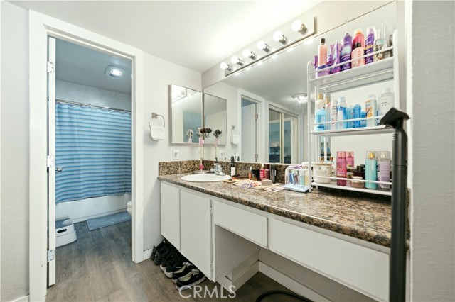 A bathroom vanity with granite countertop and a mirror, looking through an open door into a blue-curtained shower area