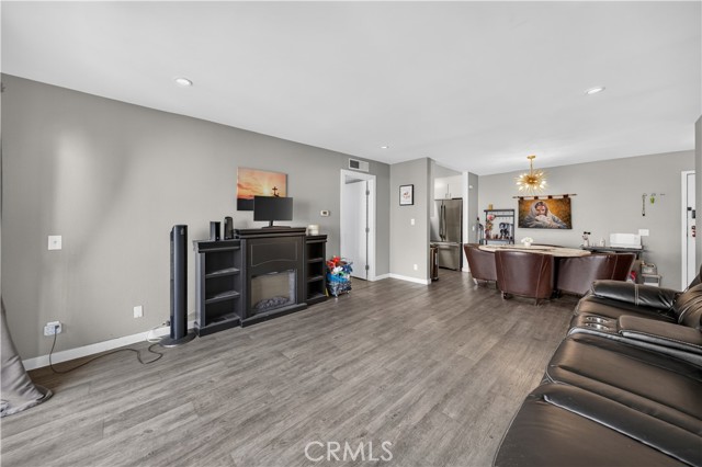 A wide angle shot of a living room with grey walls, dark wood-look laminate flooring, a fireplace console, and a dining set in the background.