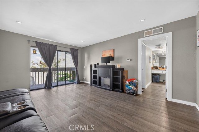 A living room with dark laminate floors, grey walls, a black fireplace unit, and a sliding glass door leading to a patio.