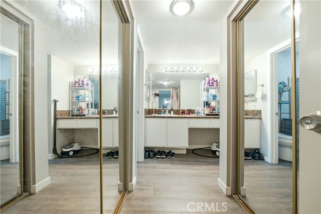 Bathroom vanity area featuring white cabinetry, granite countertop, and mirrored sliding closet doors reflecting the space