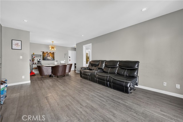 A living room with gray walls and wood flooring containing a large black leather sofa and a dining area in the back